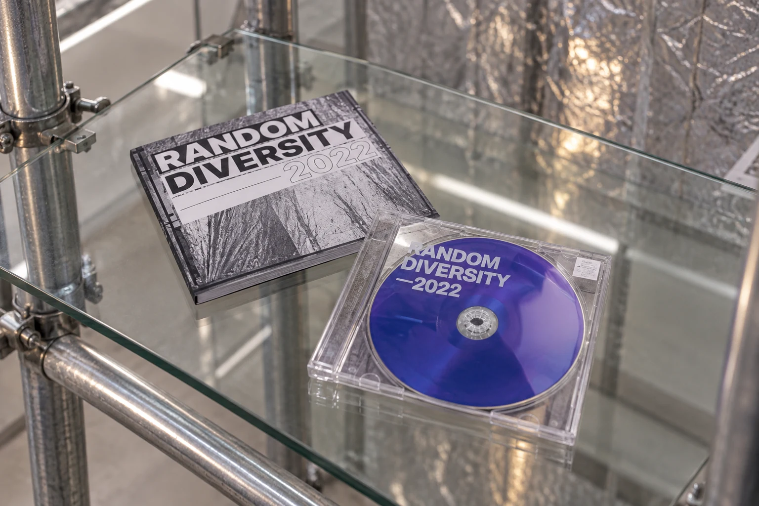 합정 Random Diversity 2022의 파란 CD와 전시 인쇄물을 유리 선반 위 정물로 재구성한 이미지